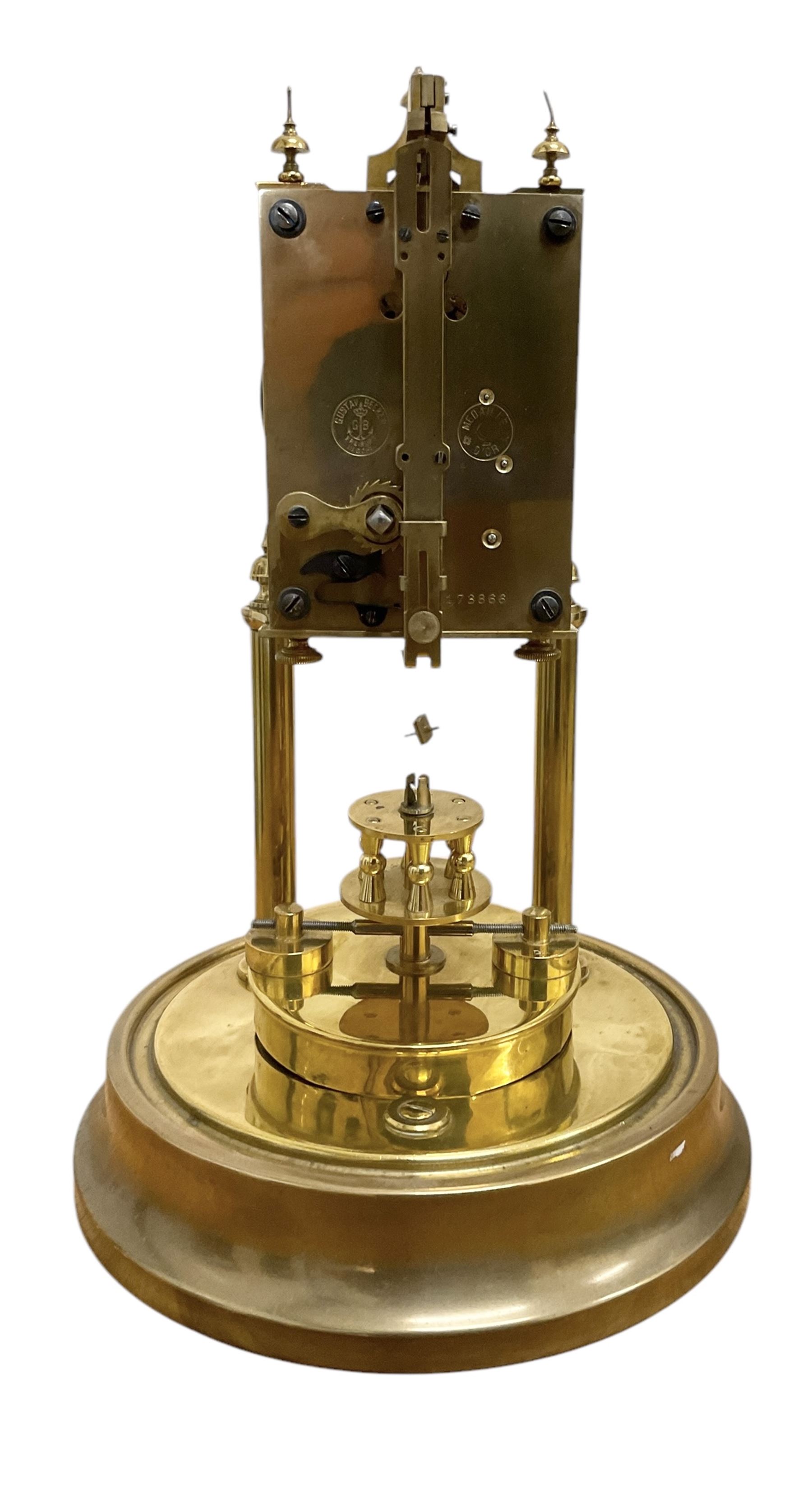 Gustav Becker - German early 20th century torsion clock, with a skeleton movement and rotary oscillating pendulum, enamel dial with Arabic numerals , minute markers and steel spade hands, on a circular brass base with a glass dome, serial No 2173866, with torsion spring complete and in place. With key.