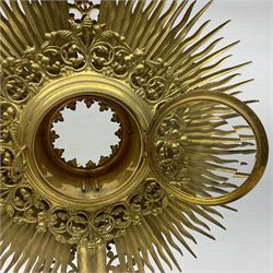 20th century gilt metal monstrance, in the Gothic revival style, with glazed aperture to centre surrounded with clear paste stones, in a pierced floral and scroll border set with coloured paste stones, within a sunburst surround, on a paste set knopped stem and similar foliate foot, H59.3cm