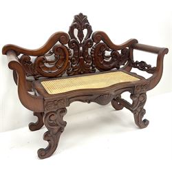 Hardwood two seat bench, floral carved and pierced back, scrolling arms, cane seat
