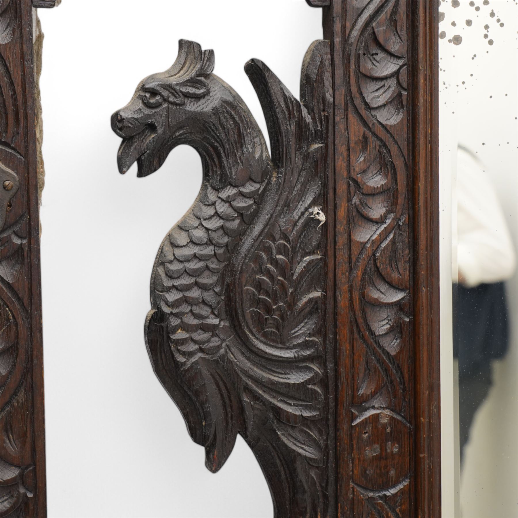 Late Victorian heavily carved oak hall stand, the scrollwork pediment with carved lion's head, bevelled mirror plate flanked by carved dragon motifs, over hinged storage compartment and umbrella stands with drip trays, on turned front supports