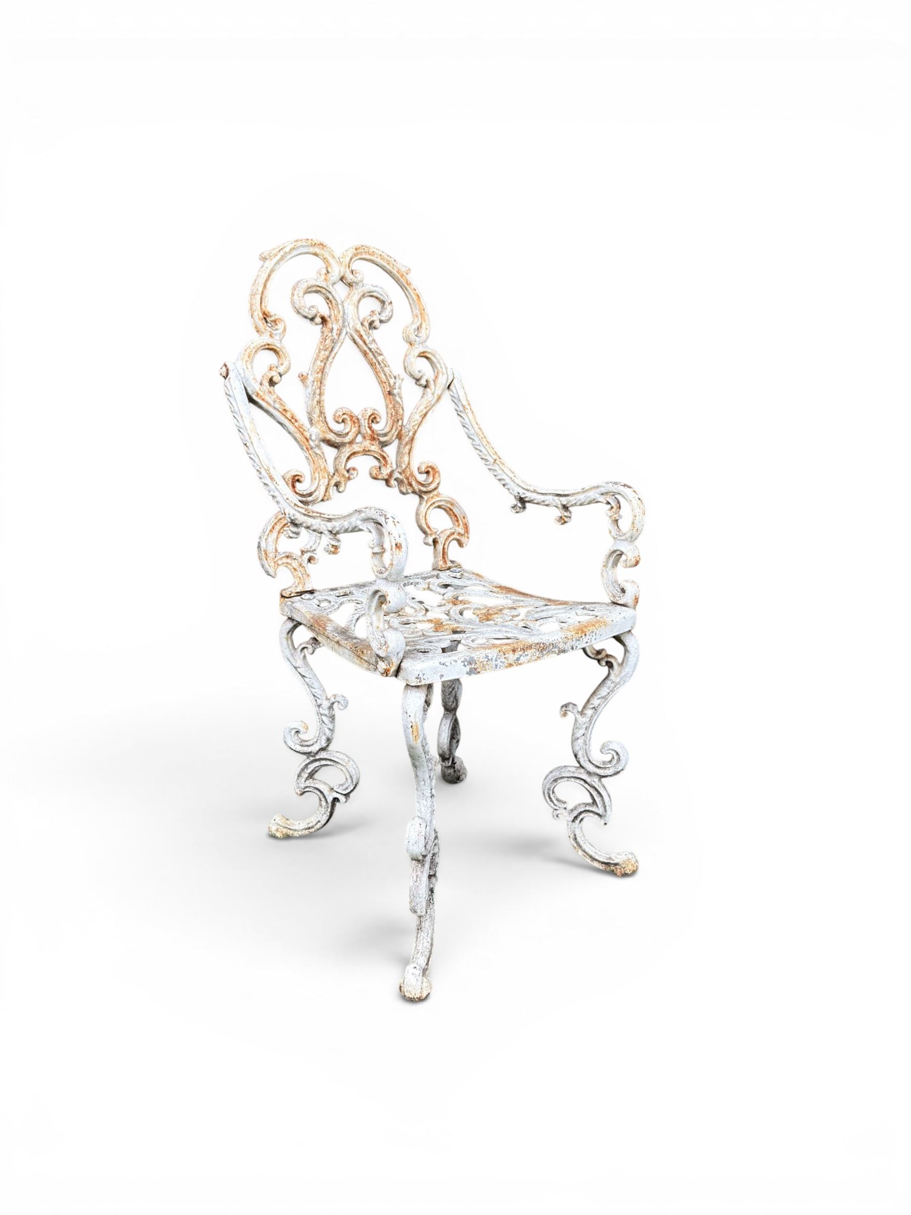 Pair of Victorian cast iron garden chairs, the ornate pierced back of scrolling foliate design, scrolling arm terminals over splayed supports formed of C and S-scrolls, in distressed white painted finish