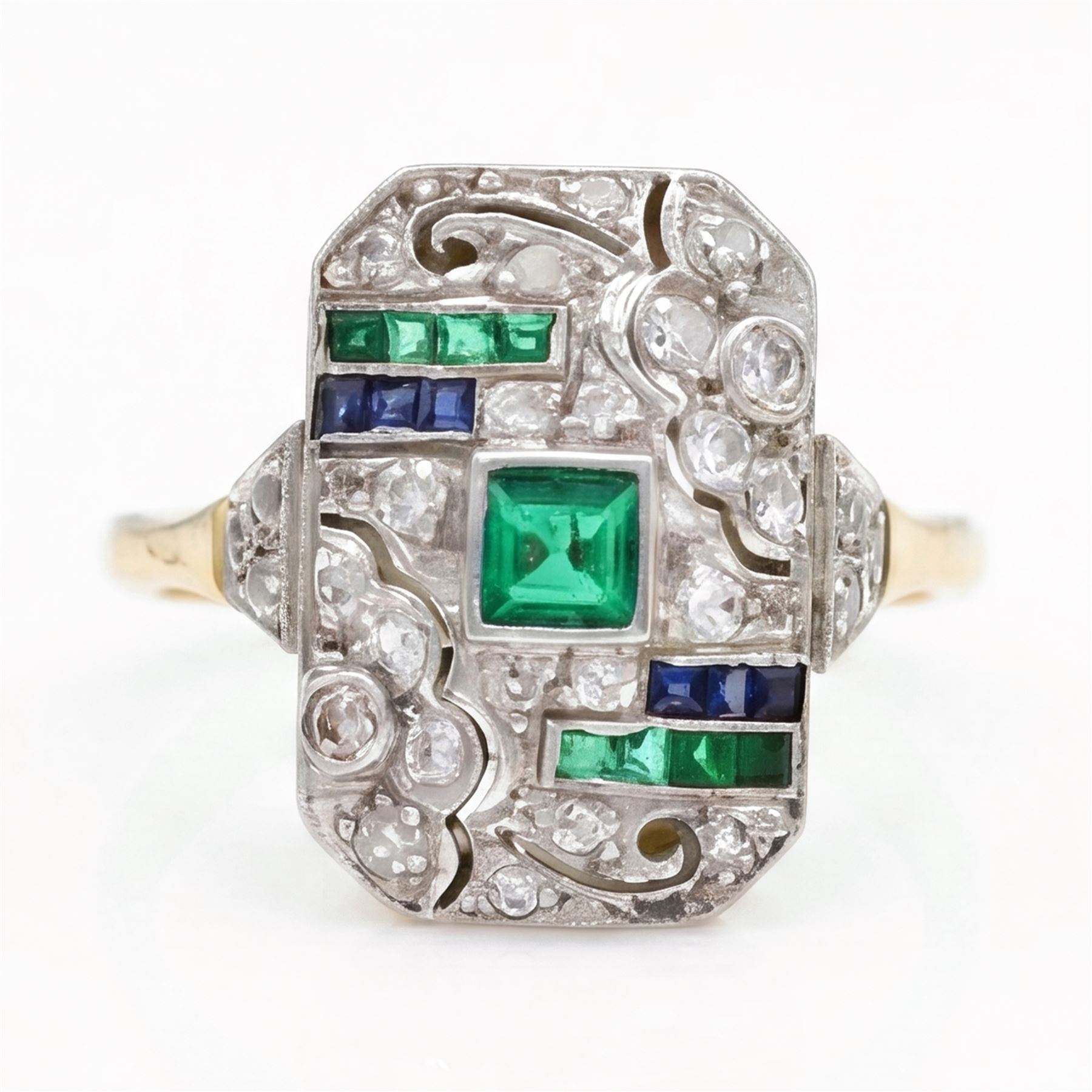 Art Deco 18ct diamond, emerald and sapphire panel ring, the rectangular floral pierced panel set with a single square cut emerald, surrounded by old cut diamonds and four rows of channel set calibre cut emeralds and sapphires, to diamond set shoulders 