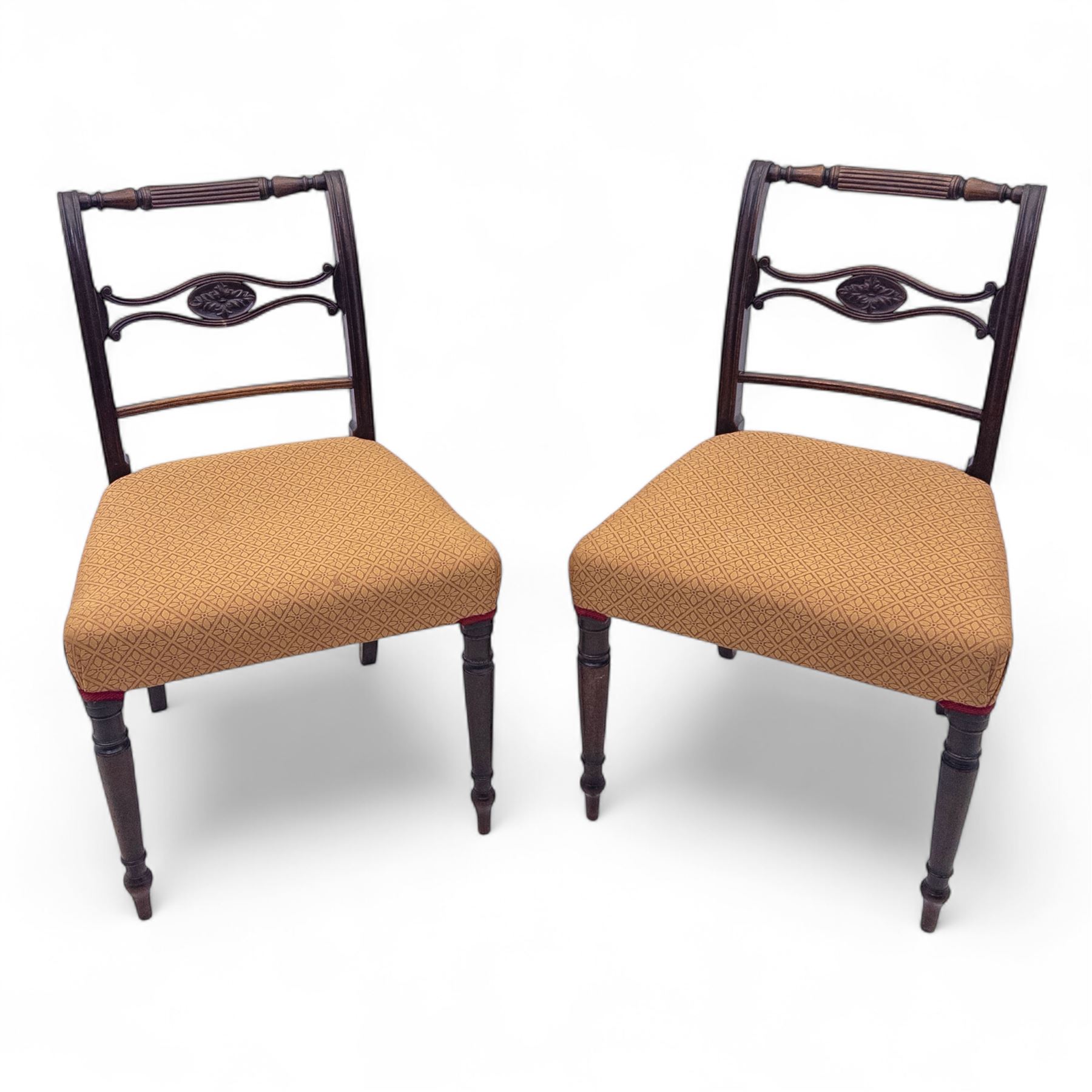 Pair of Regency mahogany side chairs, reeded bar backs centred by oval paterae, overstuffed seats upholstered in gold geometric patterned fabric, on turned tapering front supports 