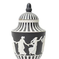 Wedgwood 20th century 'Dancing Hours' jasperware urn, the upper section decorated with a single band of neoclassical maidens in white to a black basalt ground, rising from a circular plinth decorated with foliate motifs, complete with cover with acorn finial, stamped 'Wedgwood Made in England', H25cm 