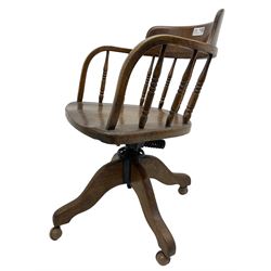 Early 20th century oak framed swivel Captain's chair, tub shaped back with turned spindle supports over saddle shaped seat, quadriform base on castors