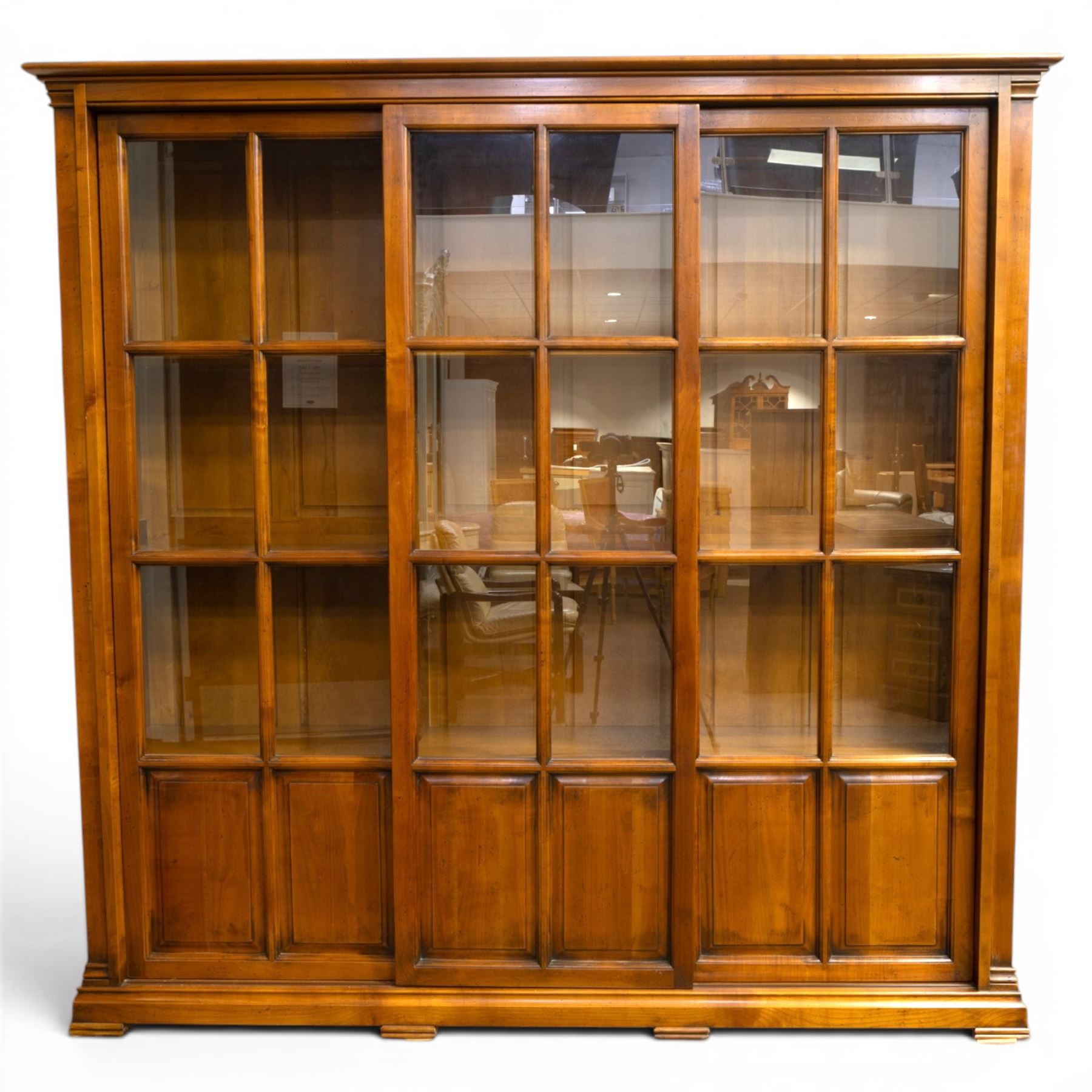 Wesley Barrel - large cherry wood bookcase, with projecting cornice and fielded panelled sides, with three sections comprising three fixed shelves, sliding glazed and panelled doors, moulded plinth base