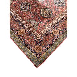 Large Persian design red ground carpet, the field decorated with multiple shaped panels surrounded by trailing leafy branches and stylised plant motifs, the guarded border decorated with shaped panels and floral pattern 