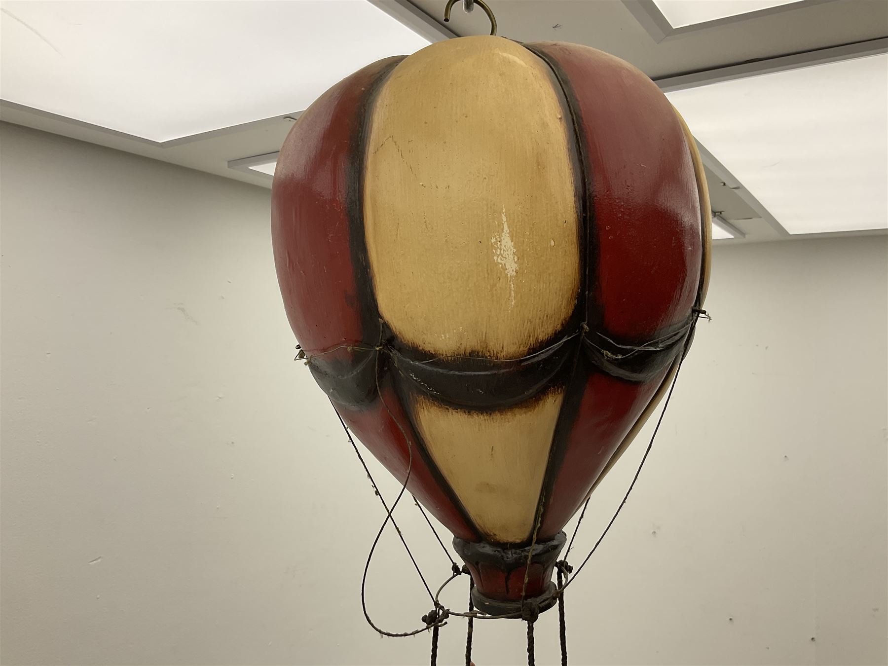 Painted wooden hanging model of a hot air balloon group, the balloon above a wicker basket complete with sandbags and figures, together with a similar example with a clown figure below, H68cm