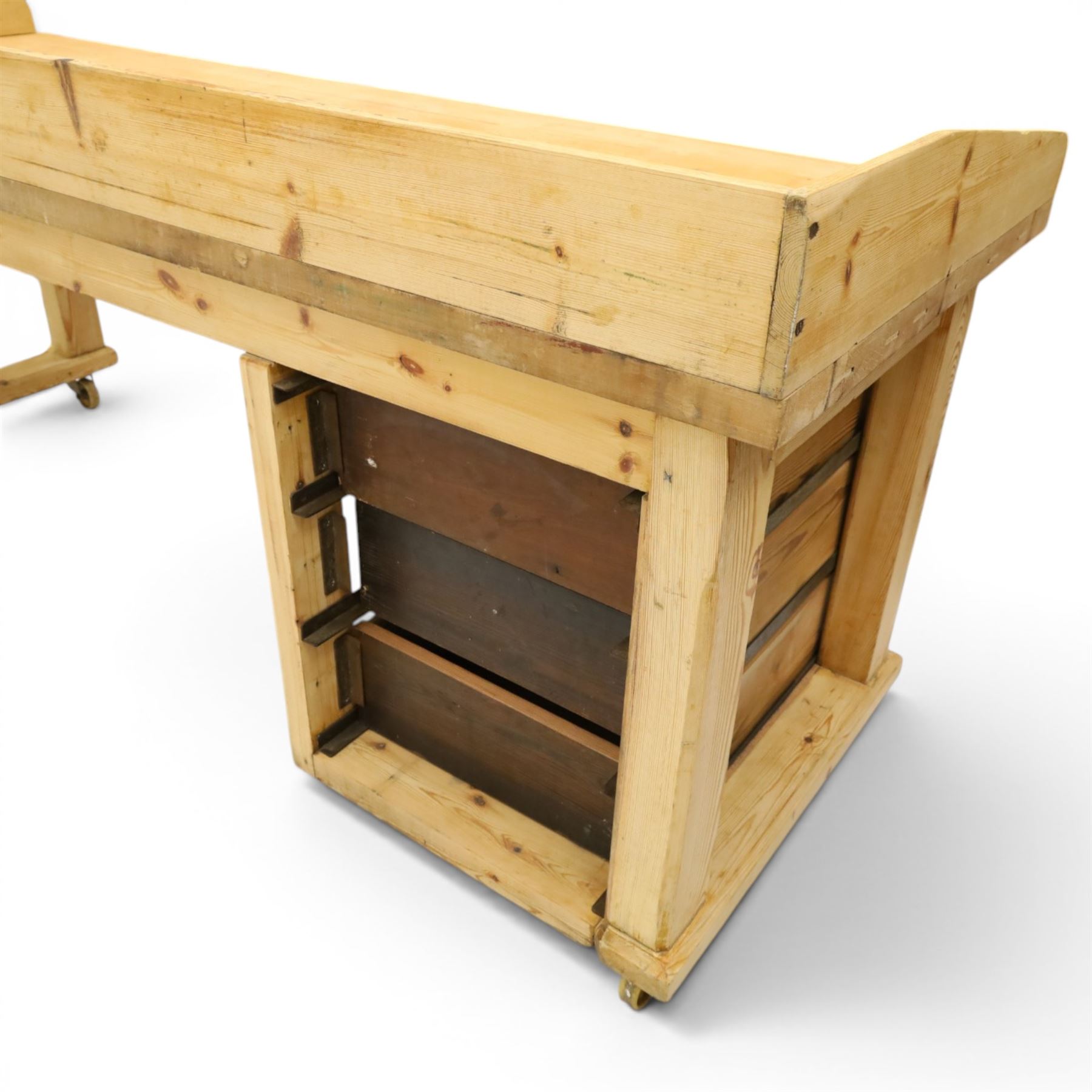 Mid-20th century pitch pine and beech bakers table, three quarter galleried rectangular plank top, three drawer pedestal with iron handles and runners, square supports with iron spandrel, raised on castors 