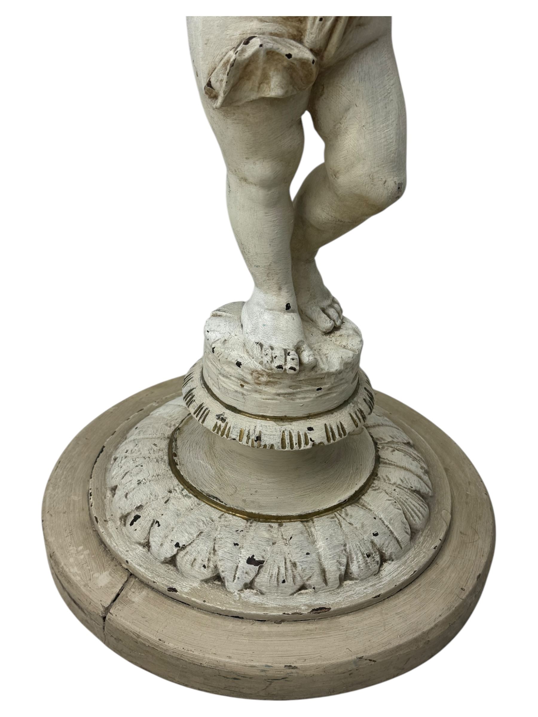 Early 20th century figural torchère, modelled as a standing putto supporting a circular top with tasselled drapery effect, raised on a circular base with foliate moulding; together with a 19th century large carved wood fragment, triangular form with high relief fruit, foliage and shell motif (H23cm, W129cm)