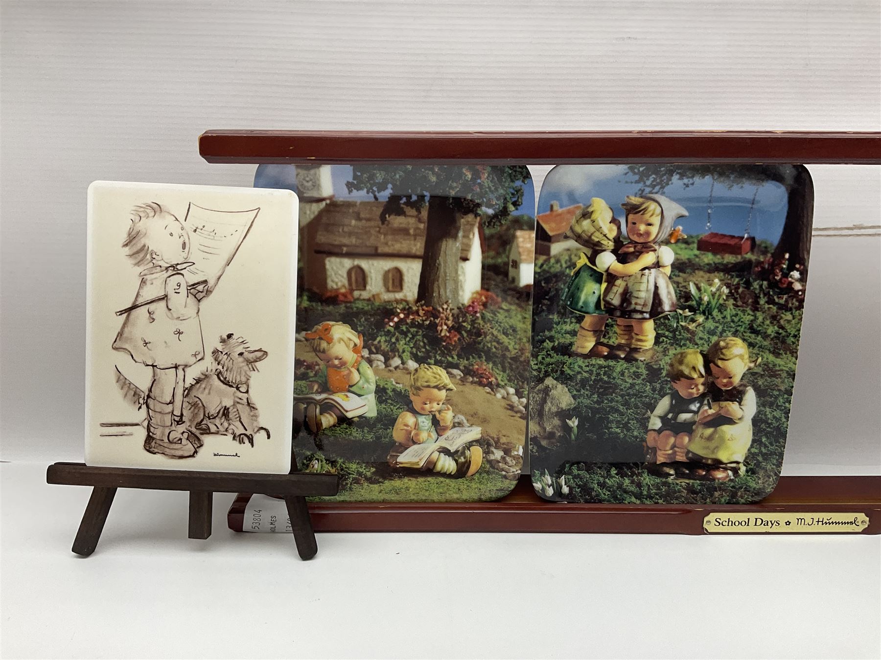 Two ceramic Hummel postcards by Goebel, both displayed on wooden easels, together nine Hummel eggs, set of four Hummel School Days plates, on wooden hanging rack, Goebel Collectors Club Member plaque etc