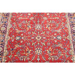 Persian Kashan crimson ground rug decorated with scrolling foliage, the indigo guard stripes with repeating stylised palmette motifs