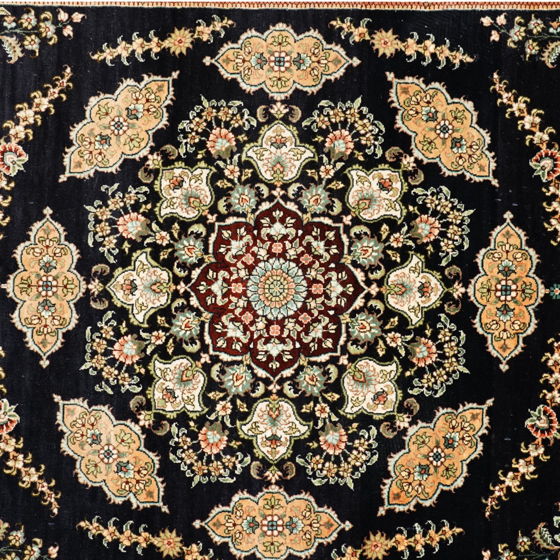 Persian-inspired Qom-style silk rug, deep indigo ground, profusely decorated with foliate motifs and a central medallion, with cotton fringe ends 