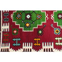 Persian Fars province crimson ground kilim rug, decorated with two rows of geometric emerald green motifs containing stylised plant designs, enclosed by an ivory and dark indigo guard band