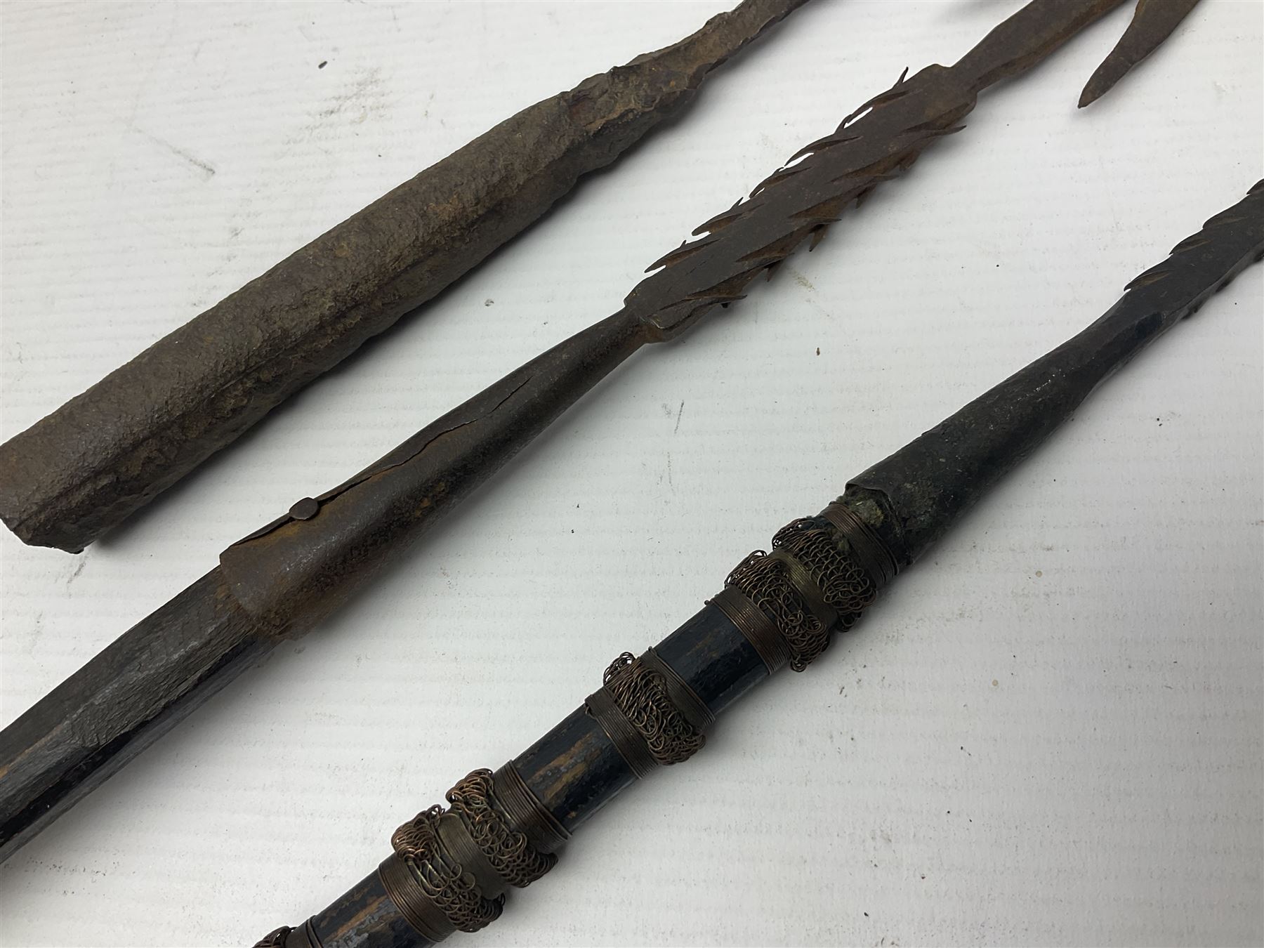 Native hand forged iron fishing spear, the V-shaped head with barbed neck and hewn haft L171cm; and two other hand forged iron spear heads, one with remains of copper bound haft (3)