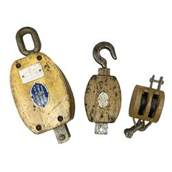 Three ship pulleys comprising wooden block double with swivel eye marked 'wooden block 240mm double rope: 22mm',  wooden block double with upset shackle and wooden block with stiff swivel hook, largest example L50cm