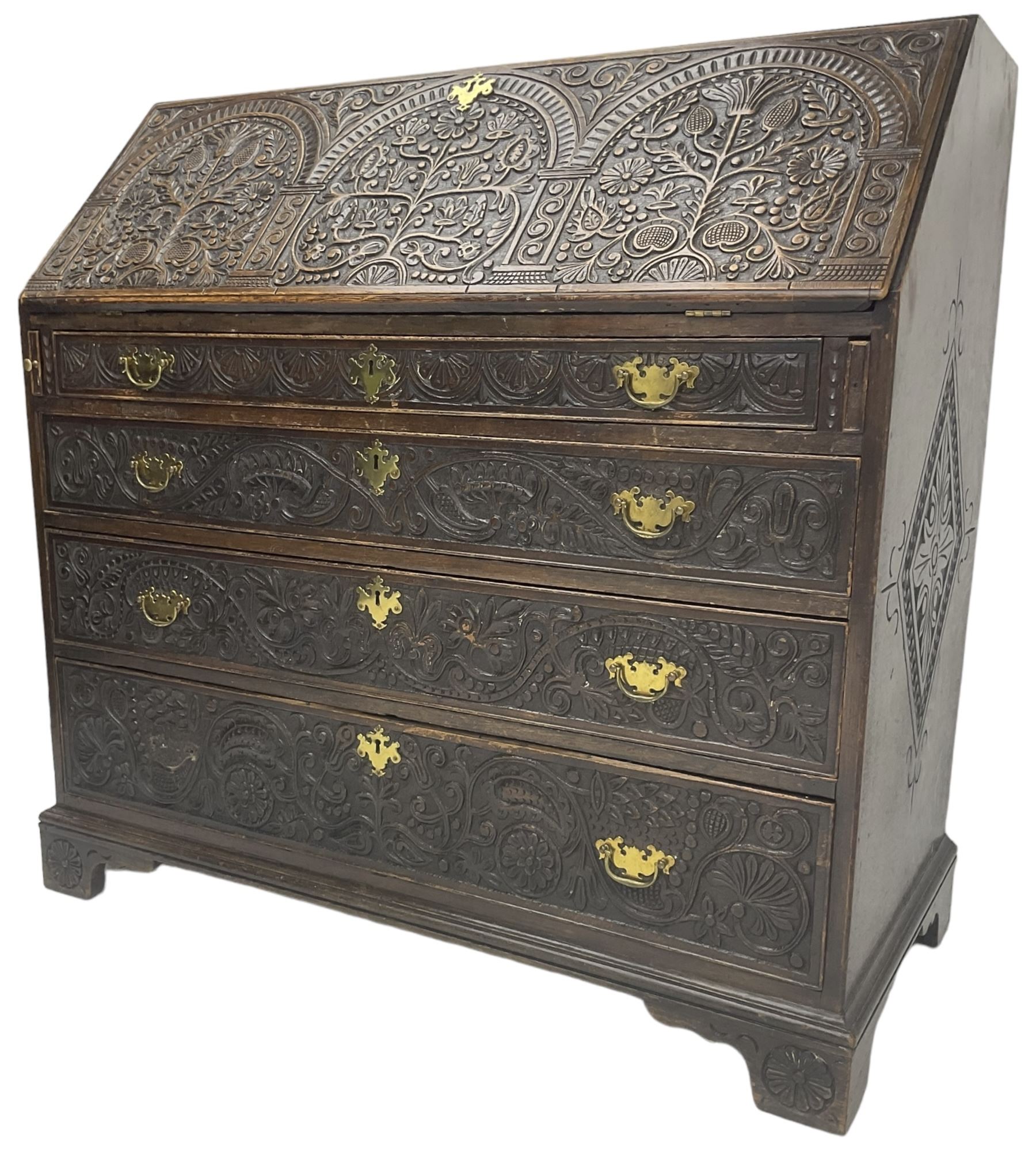 18th century heavily carved oak bureau, the fall front relief carved with three arches enclosing plants and flower head decoration, the interior fitted with pigeonholes, drawers and cupboard, four graduating cock-beaded drawers below, carved with lunettes and trailing foliage decoration, on bracket feet