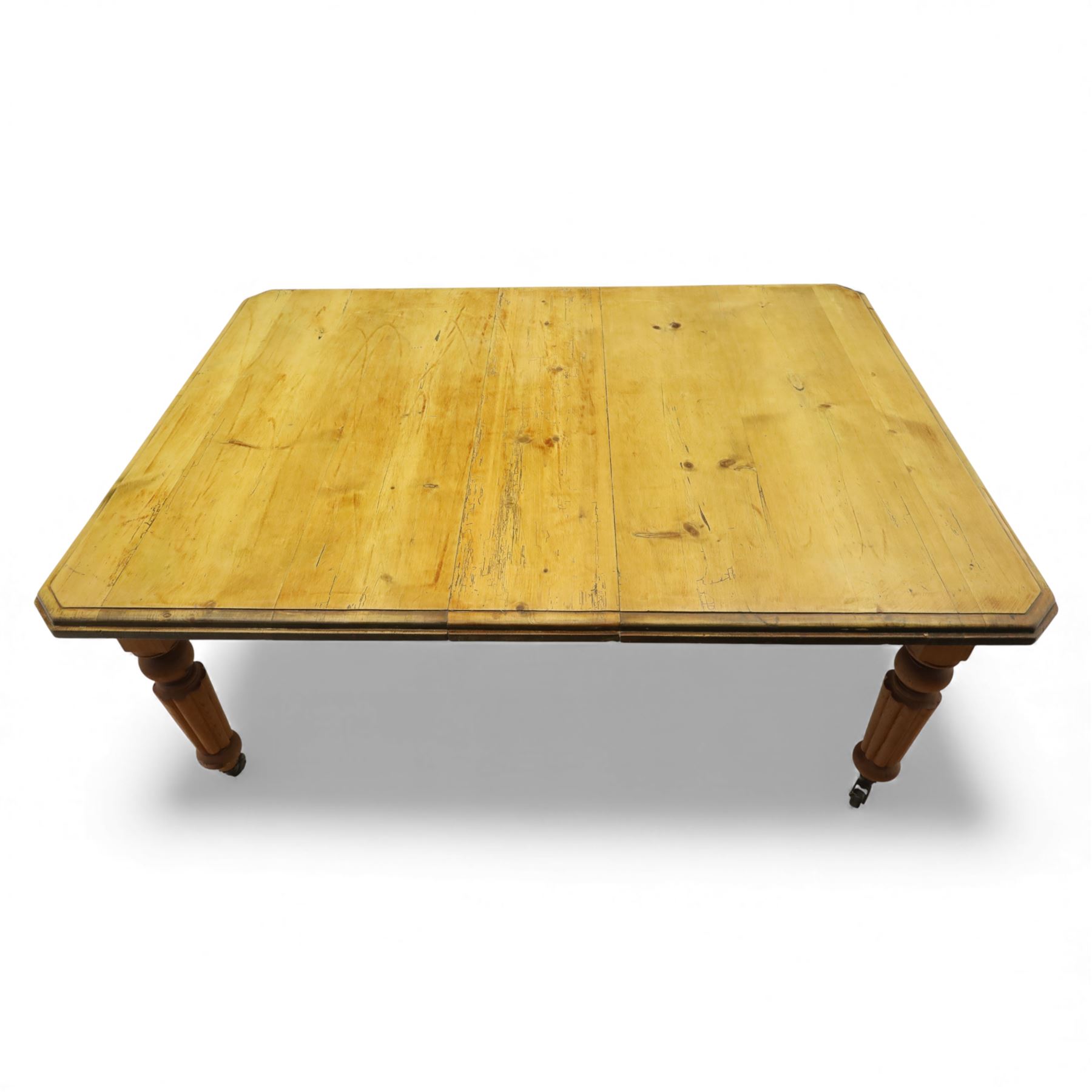 Early 20th century stripped pine kitchen table, the rectangular planked top with moulded edge and canted corners, upon stained pine turned and fluted legs with castors