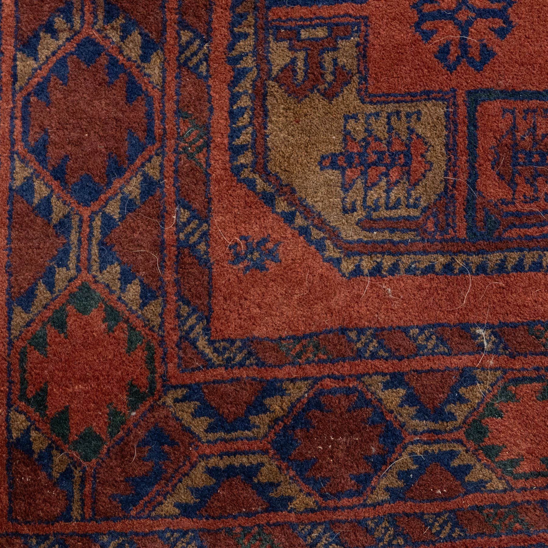 South East Persian Afshar hand-knotted rug, red ground decorated with a geometric design of octagonal medallions and incorporating stylized motifs in tones of indigo and dark brown within geometric borders, with fringe ends  