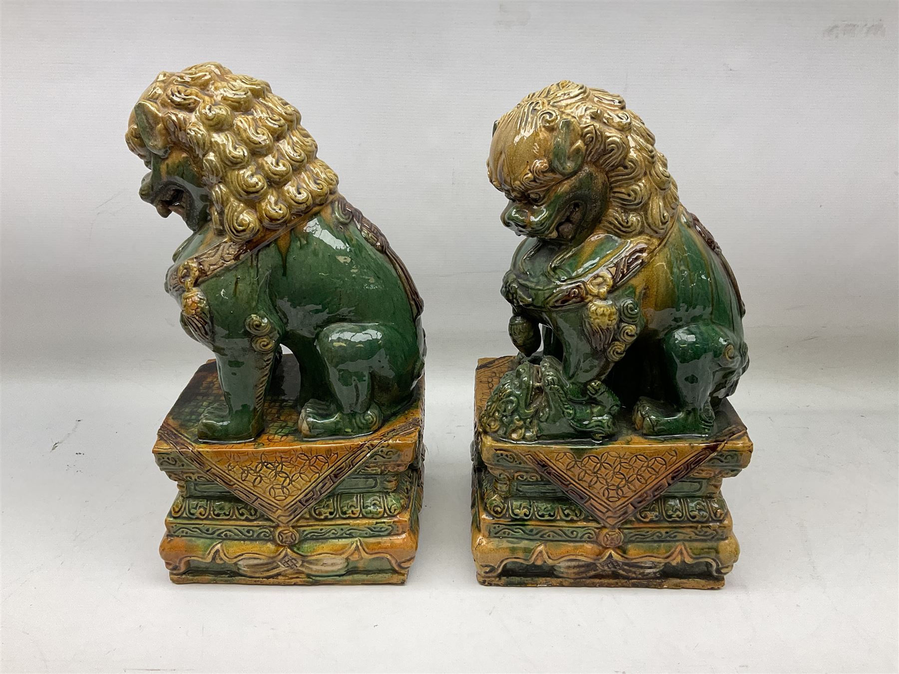Pair of Chinese Temple Lions or Dogs of Foo, modelled in seated post, one with one front paw resting upon a ball, the other upon a cub, each upon stylised plinth base, H44cm