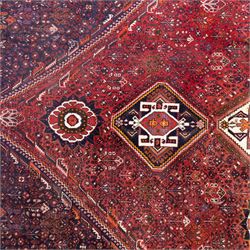 Qashqai wool carpet, red diamond-shaped field decorated with three stepped pole medallions, floral rosettes and scattered stylised motifs, within dark blue spandrels and multiple geometric guard borders