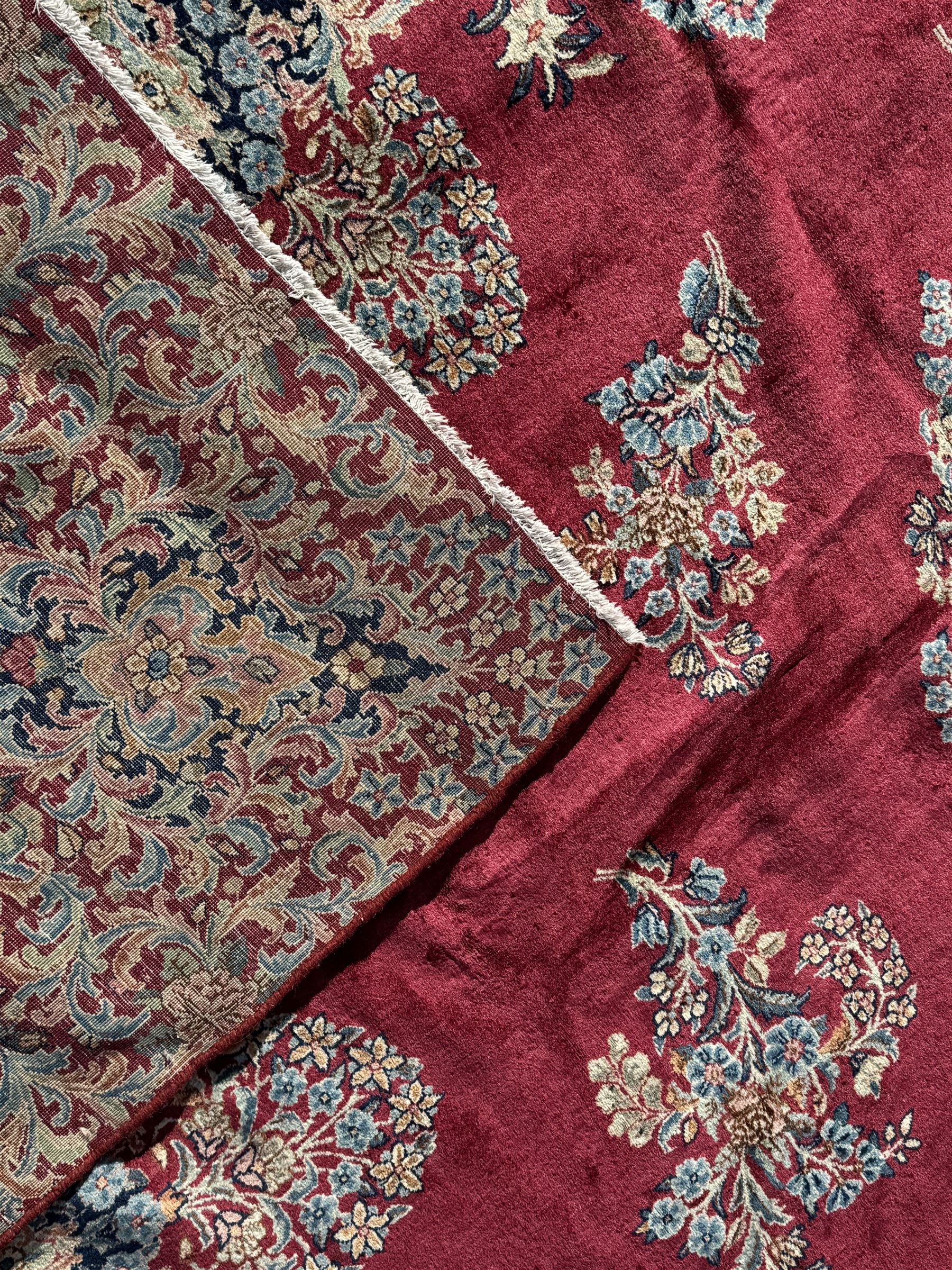 Persian Kirman carpet, the bold ruby field hosting a multi-lobed central medallion, embellished with scrolling vines and floral sprays, edged by layered borders and trimmed with short fringe