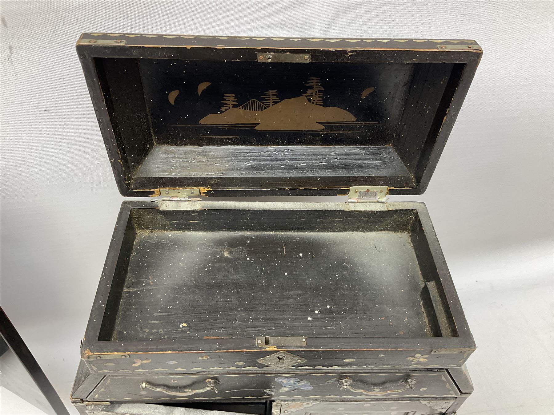  Late 19th / early 20th century Japanese lacquered table top cabinet, heavily decorated with mother of pearl inlay depicting blossoming branches, flowers and birds, the two hinged doors between longer drawers opening to reveal interior fitted with four short drawers, with lift up hinged canted lid, H28cm D9.5cm W23cm, together with mother of pearl inlaid miniature folding screen, dish decorated with walking figures with crimped edge, boxes decorated with flowers, birds and gilt etc