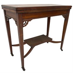 Edwardian inlaid mahogany games table, the rectangular fold-over swivel top decorated with central shell motif inlay and ebony stringing, raised on tapering supports united by shaped X-stretcher and undertier