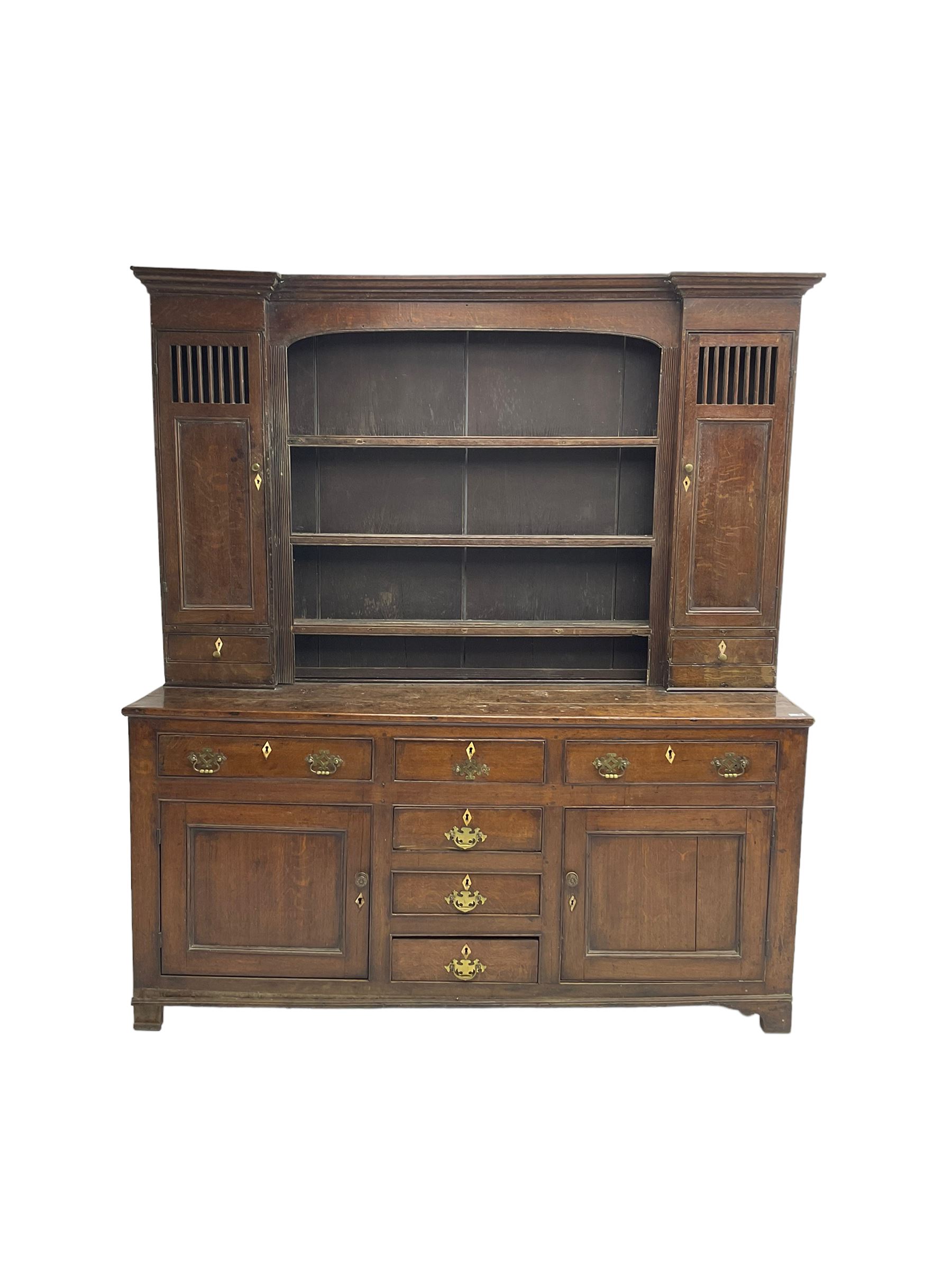 George III oak dresser, projecting cornice over three tier plate rack flanked by reeded uprights and two cupboards, enclosed by slatted and panelled doors above small drawers, the lower section fitted with six drawers and two cupboards, on bracket feet