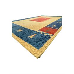Contemporary 'Royal Garden' wool pile rug, central cream field with a smaller red rectangular panel containing scattered animal and geometric motifs, bordered by a wide indigo band decorated with stylised figures, animals, and tree motifs