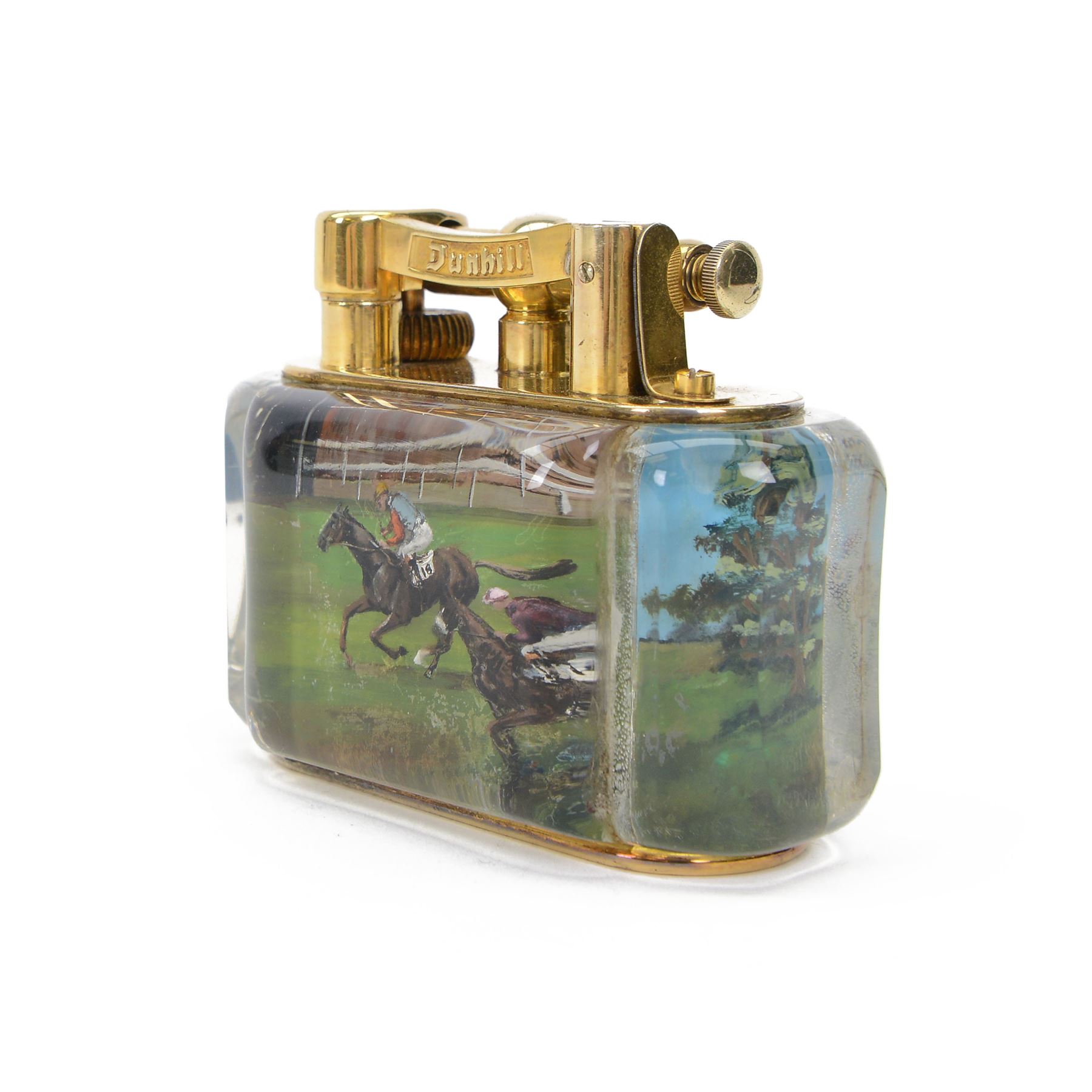 Rare one off special commission Dunhill Sporting Horse Racing half-giant 'Aquarium' table lighter, circa 1955, the lucite panelled body engraved in reverse intaglio technique and hand-painted with Nicholas Nickleby in action, winner of the Royal Hunt Cup, Ascot June 1955, the reverse with jockey Willie Snaith mounted upon Nicholas Nickleby, the gold plated top with arm stamped Dunhill Reg. No 737418, the base stamped DUNHILL LIGHTER, H7.5cm W10cm D5cm

Provenance:
Commissioned by the owner of Nicholas Nickleby, the lighter was gifted to Colin Hetherton, a young veterinary surgeon whose intervention saved Nickleby from certain retirement. Hetherton’s expert care and persistence brought the horse back to full health, culminating in a win that stunned the Ascot crowd.