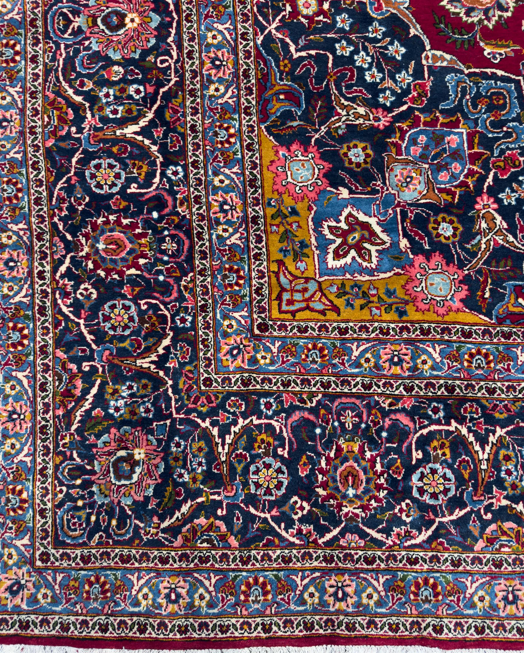 Central Persian Kashan hand-knotted carpet, madder red field with an intricate design of scrolling vines, palmettes, and rosettes with a central lobbed medallion with pendant motifs in shades of blue and ivory, and spandrels all within a blue-ground border of palmettes and flowerheads between multiple guard borders, 450cm x 335cm 