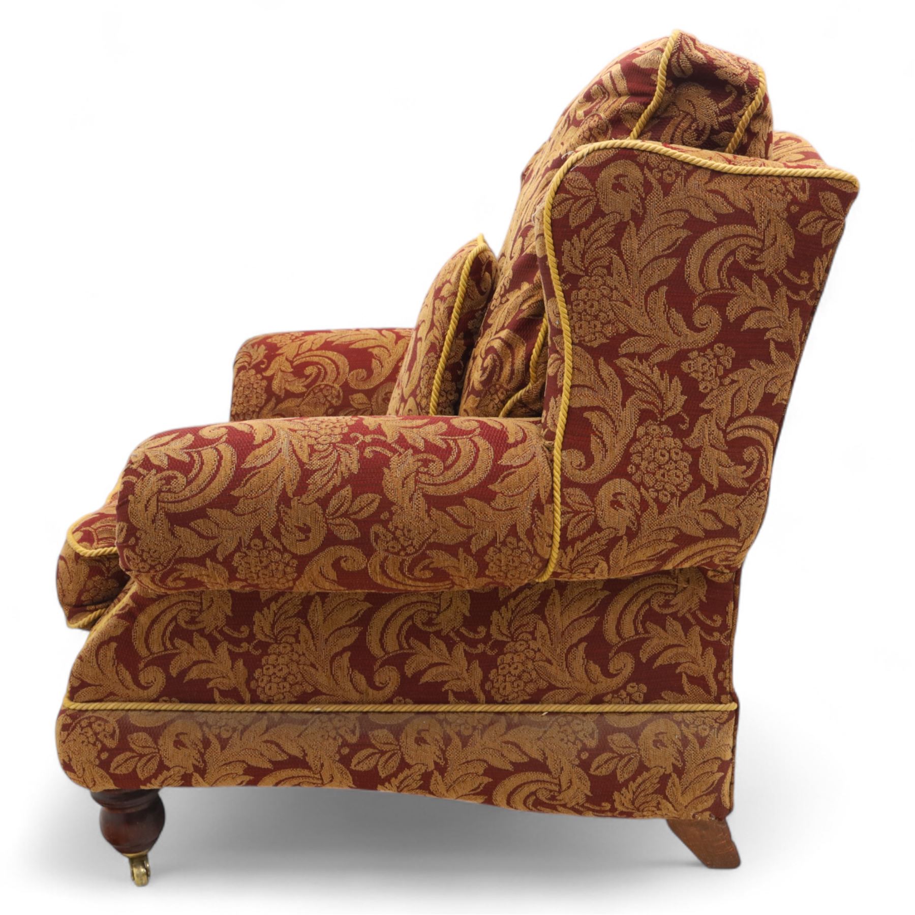 Duresta – pair of armchairs, upholstered in red and gold damask fabric with piped edges, scroll arms and loose feather-filled cushions, raised on turned wooden feet with brass castors