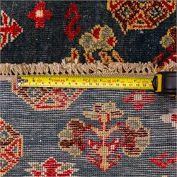 North East Persian Turkoman hand-knotted rug, deep teal blue field decorated with repeating rows of stylized octagonal guls and cruciform tribal motifs arranged in a lattice formation, enclosed composition featuring angular devices and reciprocal motifs, with cotton fringe ends