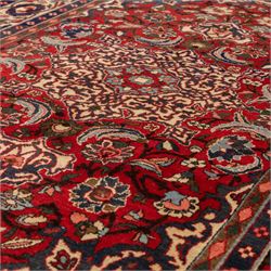 Central Persian Isfahan hand-knotted rug, madder red field, with elaborate central medallion with pendants and scrolling arabesques, palmettes and stylized floral sprays arranged in a densely ornamented ground of classical Safavid inspiration, ivory border with a continuous vine scroll of palmettes and rosettes, flanked by multiple guard stripes in navy and red with geometric and floral motifs, with cotton fringe ends 