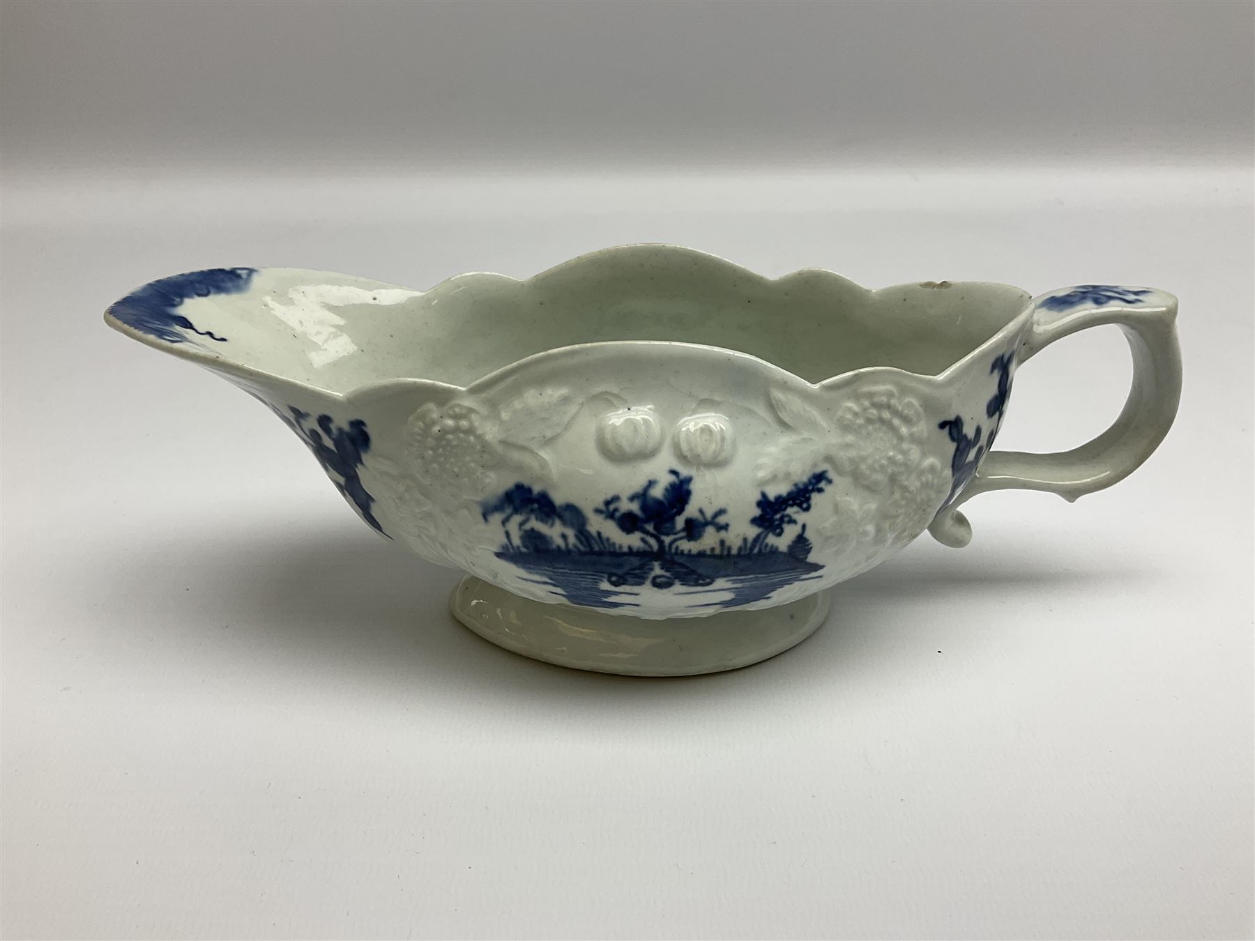 Large 18th century Lowestoft sauce boat, circa 1770, the body decorated with Hughes type floral moulding, and painted in underglaze blue with an Oriental landscape, and foliate sprigs, L23cm
