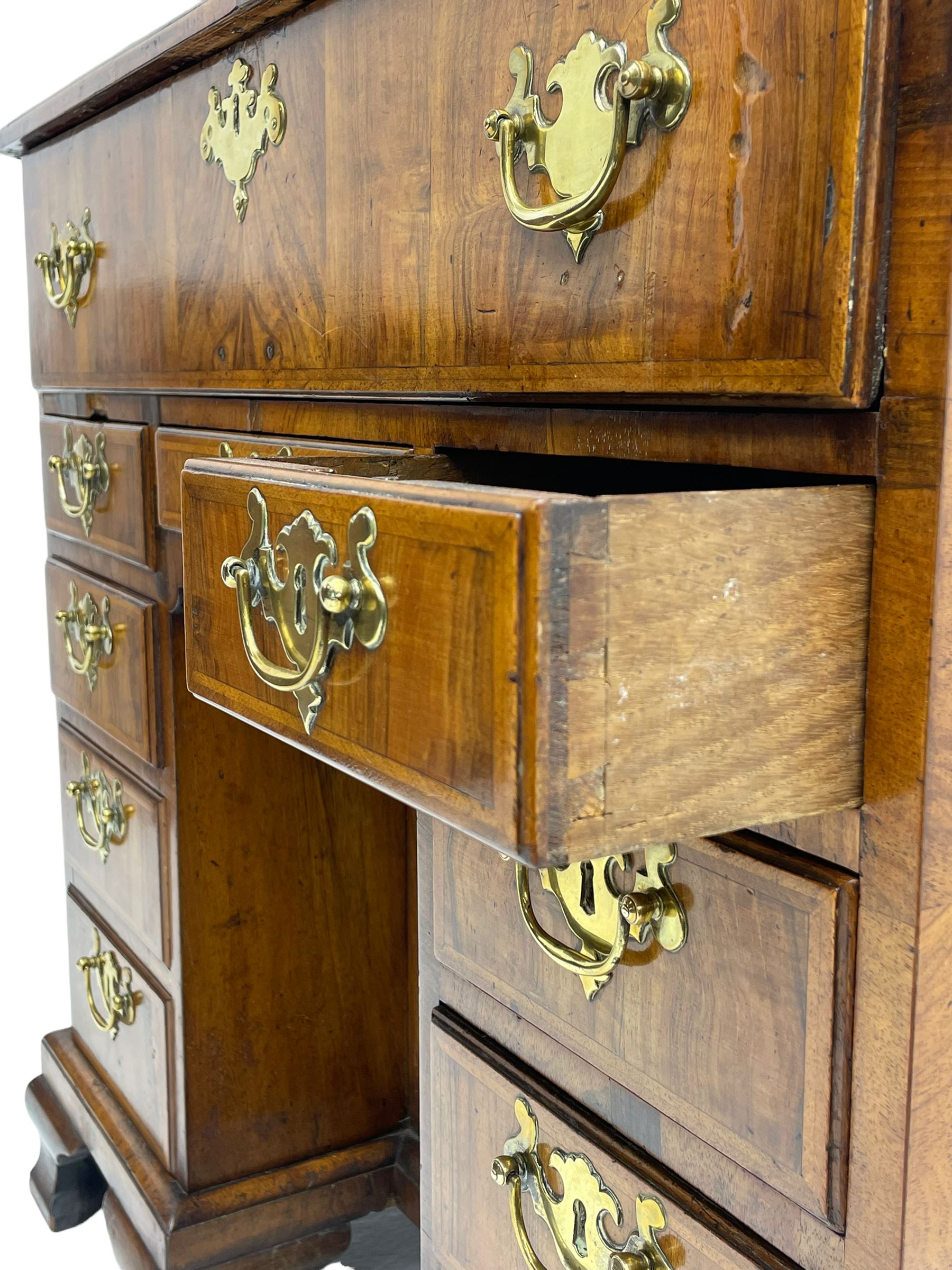 Early 18th century Queen Anne figured walnut kneehole desk with secretaire drawer, moulded and book matched top with walnut band, the top drawer with fall front enclosing small drawers and pigeon holes, fitted with nine drawers and central recessed cupboard, on ogee bracket feet