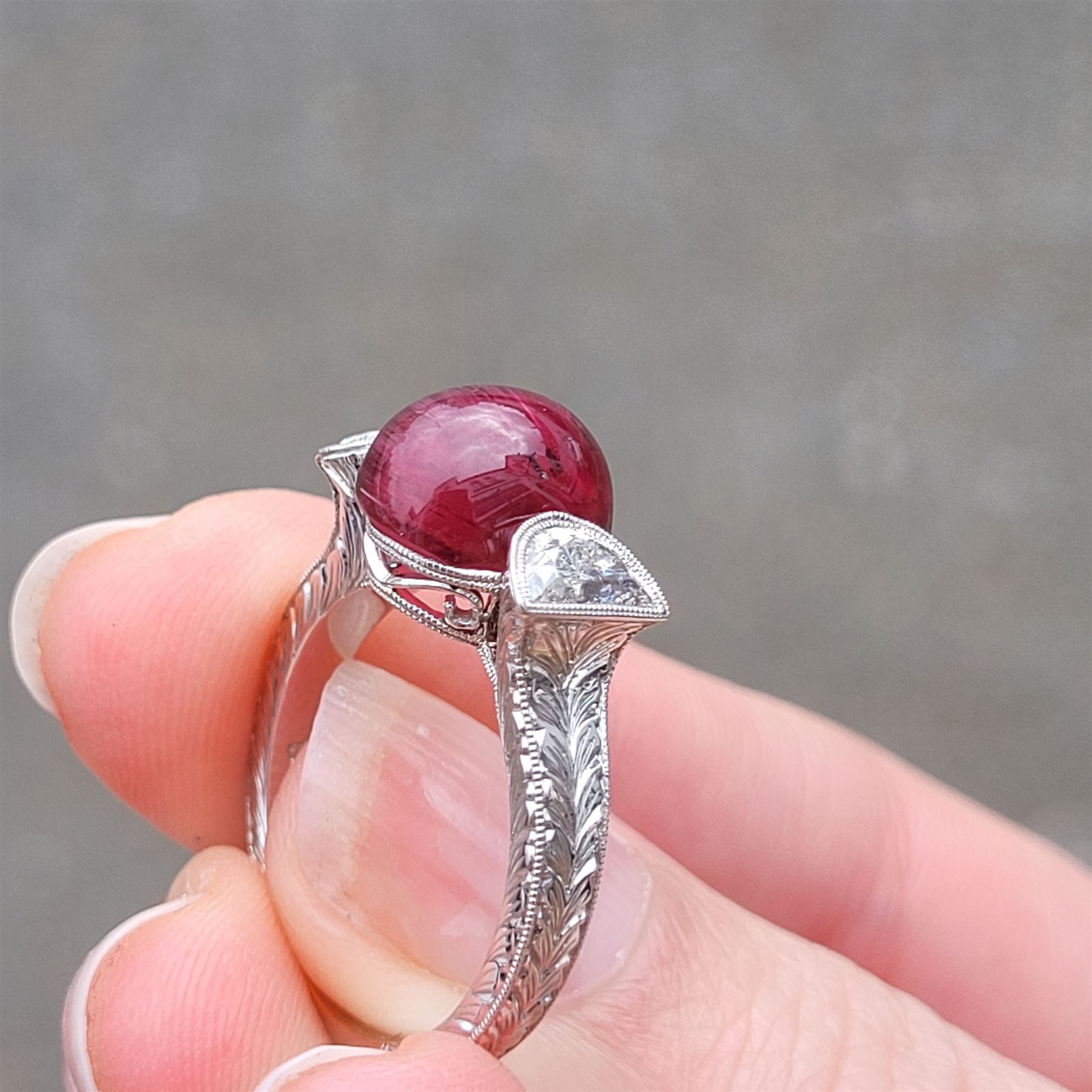 18ct white gold pink tourmaline and diamond ring, single oval cabochon cut tourmaline of approx 4.75 carat, set with a half moon cut diamond either side, to engraved laurel leaf design shoulders
