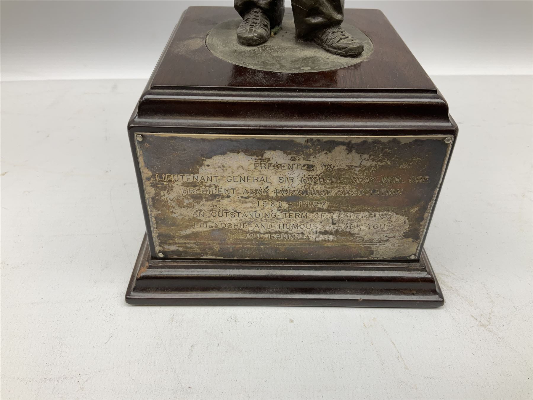 Presentation bronzed figure of a paratrooper by Peter Hicks mounted on a mahogany plinth with plaque inscribed ' Presented to Lieutenant General Sir Michael Gray KCB OBE President Army Parachute Association 1981-1987 An Outstanding Term of Leadership Friendship and Humour. Thank You All Ranks A.P.A.' H28cm; a brass Pegasus plaque H12cm; and small quantity of colour photographs and prints of military related paintings