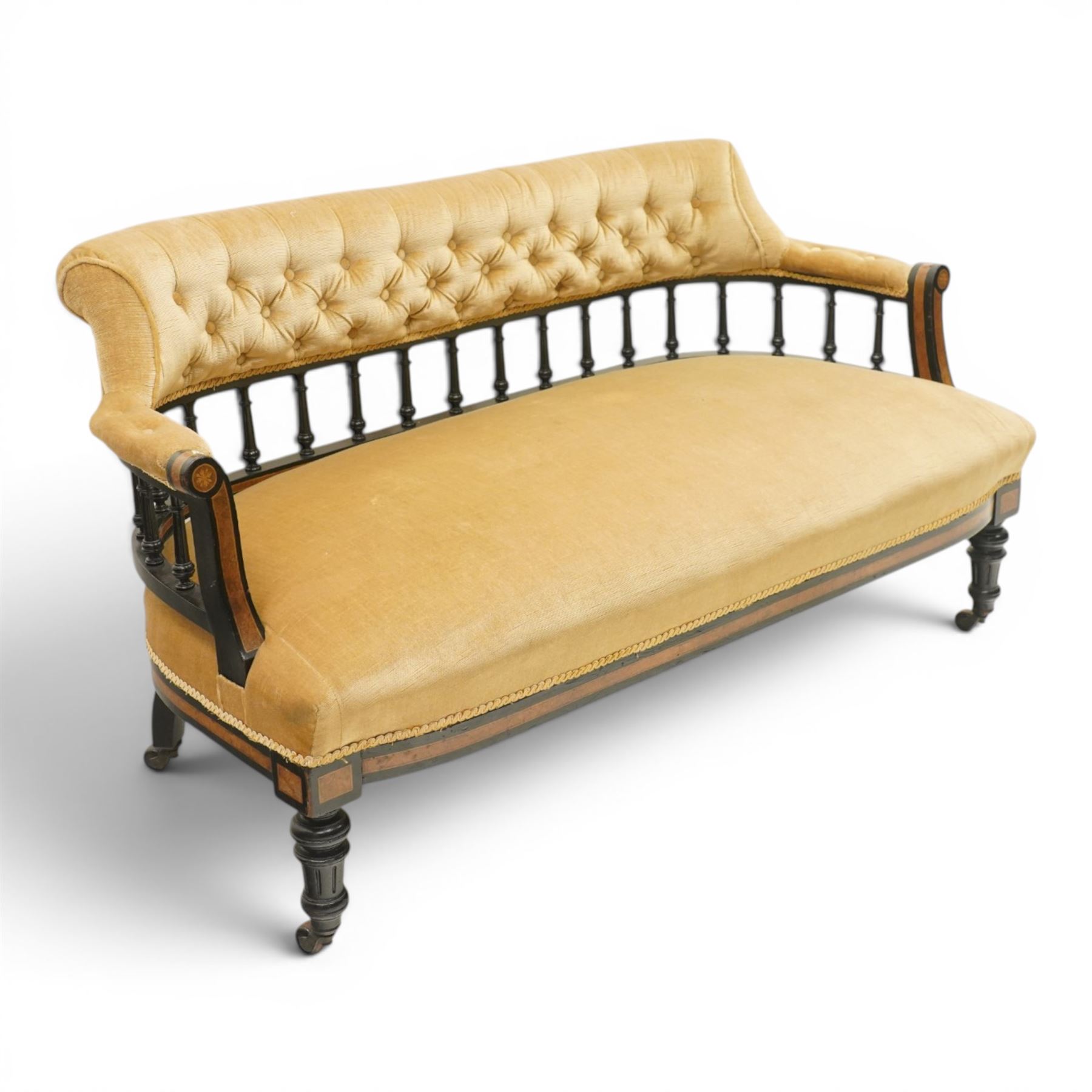 Late Victorian Aesthetic Movement settee, with buttoned upholstered roll-over back and arms, open spindle gallery frame with turned uprights, stuff-over seat, on shaped ebonised supports