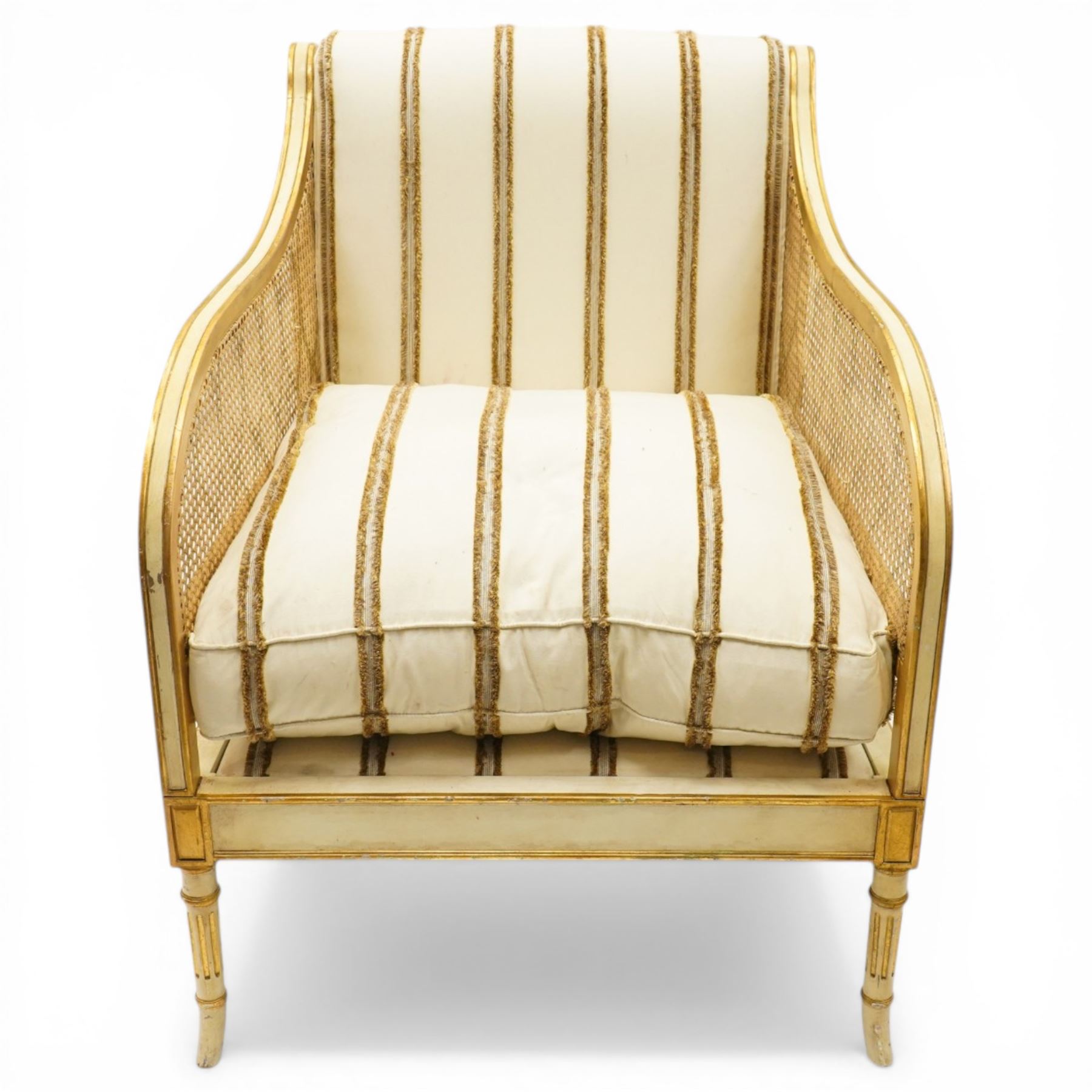 Louis XV design cream painted and parcel-gilt bergere armchair of large proportions, high scrolled back over canework arms, upholstered in striped fabric with over-stuffed loose seat cushion, on fluted supports