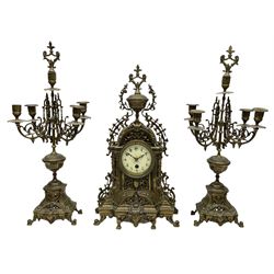 A late 19th century profusely decorated brass cased timepiece mantle clock with two matching five light candelabra, break front case raised on cast feet with decorative scroll work and a shaped urn to the pediment, eight-day spring driven French timepiece movement with an enamel dial, steel fleur di Lis hands, Roman numerals and minute track, egg and dart slip within a flat glazed bezel. With Pendulum.

