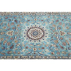 Central Persian Nain hand-knotted carpet, soft sky blue ground with central cusped medallion of radiating palmette form, issuing scrolling vine work, arabesques, and delicate floral sprays, spandrels of conforming design, main border of ivory ground decorated with scrolling vine work palmettes and stylized floral motifs, flanked by narrow guard stripes, with cotton fringe ends 