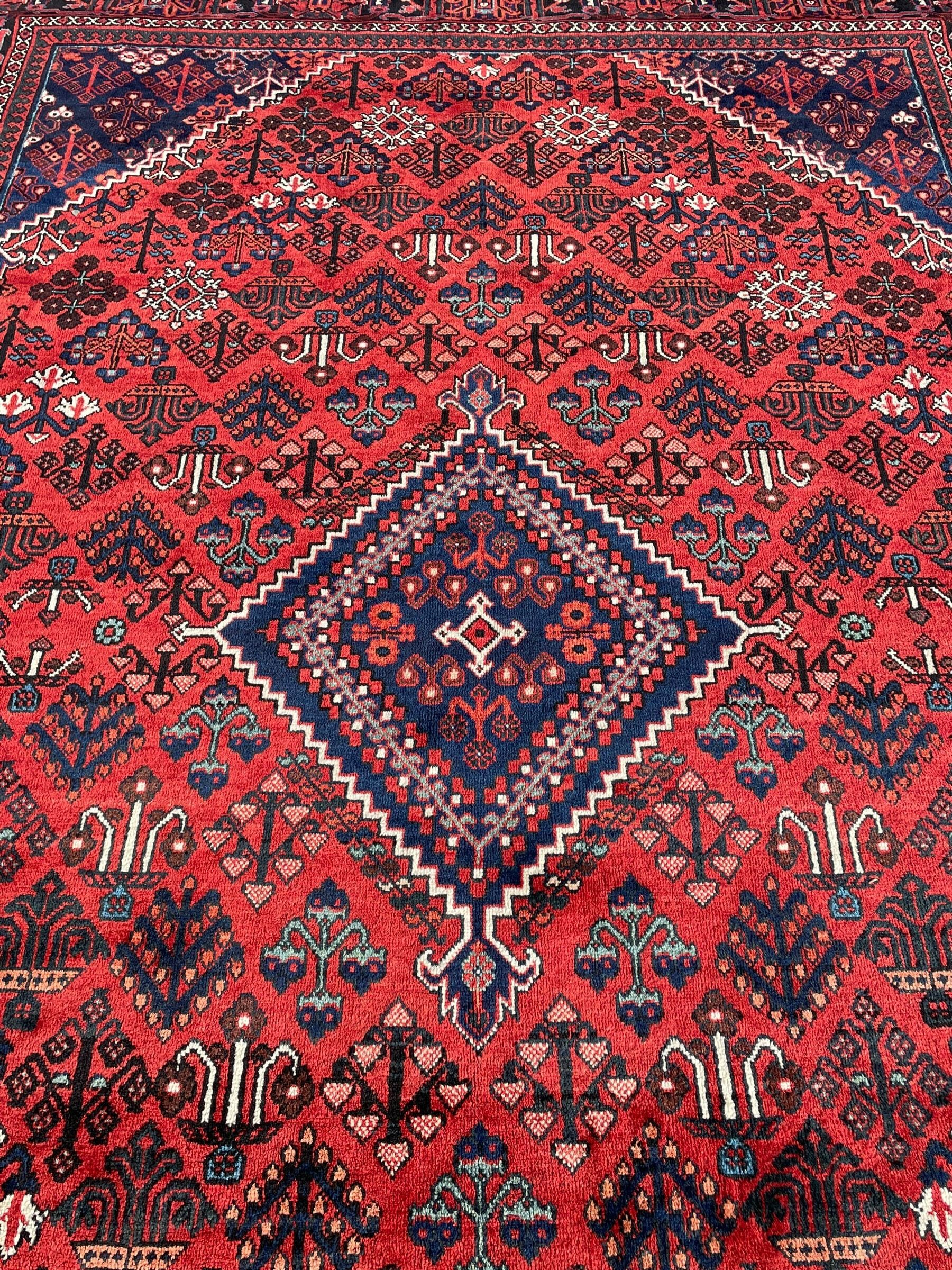 Persian Joshaghan crimson ground rug, stepped lozenge medallion surrounded by repeating foliate lozenge motifs, the border decorated with stylised plant motifs, within geometric guard stripes