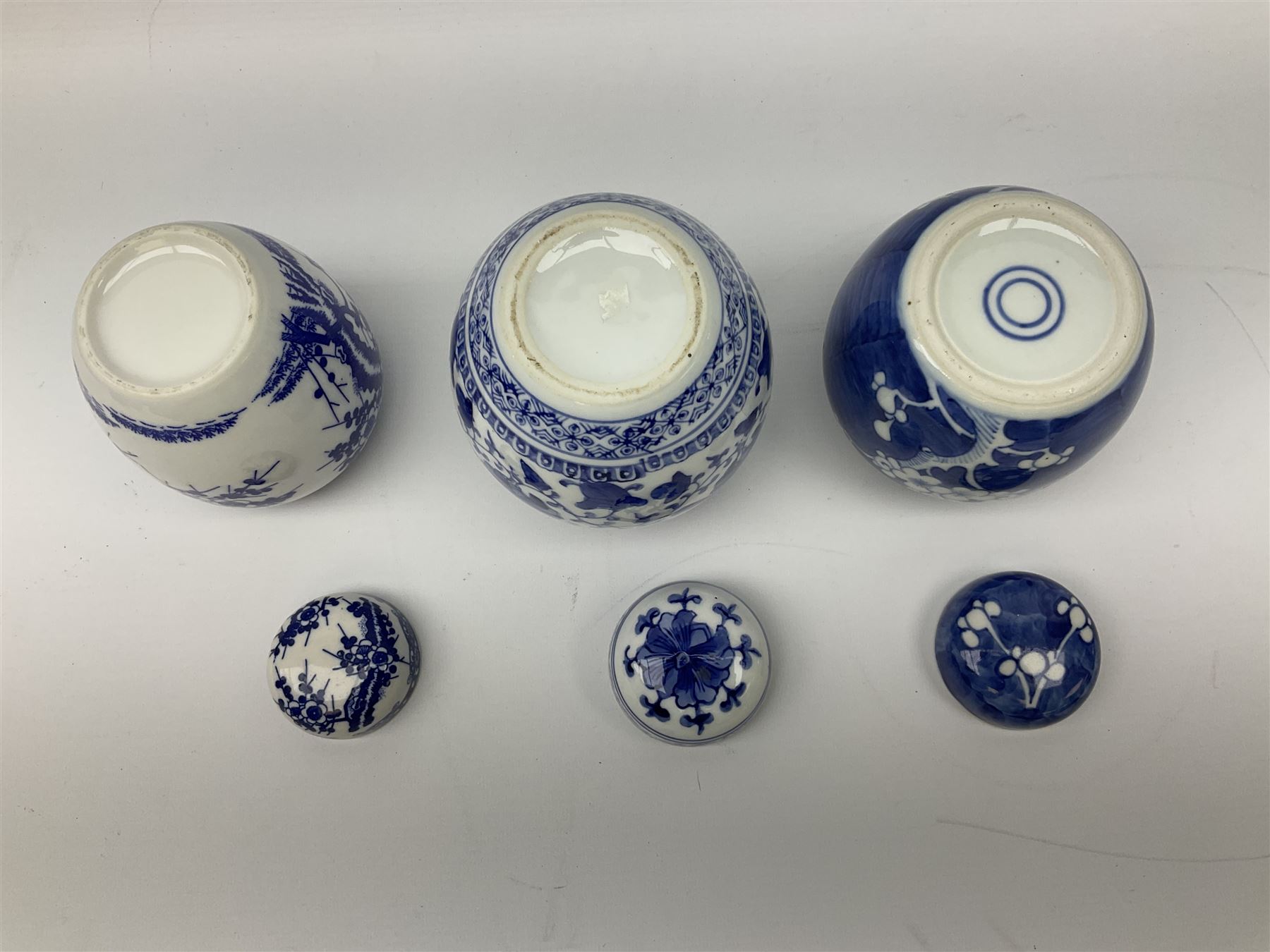 Six Chinese ginger jars, predominantly of blue and white design decorated with blossoming branches, all with lids, housed on various hardwood carved stands, some with character marks beneath