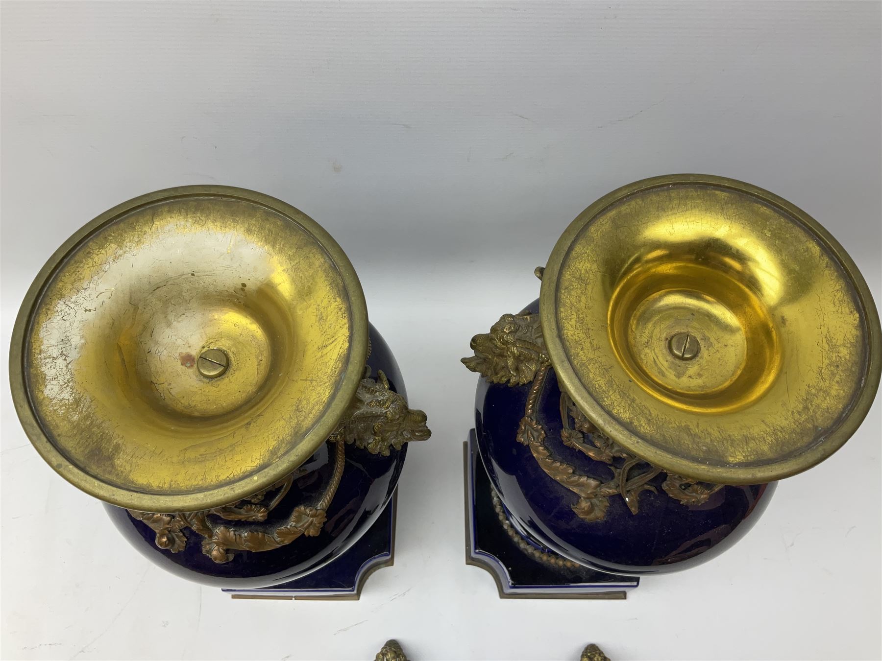 Pair of French large cobalt blue lidded urns, probably 19th century, the body decorated with ormolu ram's heads and ornate foliate design, the domed cover with brass berry finial, raised upon pedestal base with beaded decoration upon shaped plinth, H52cm