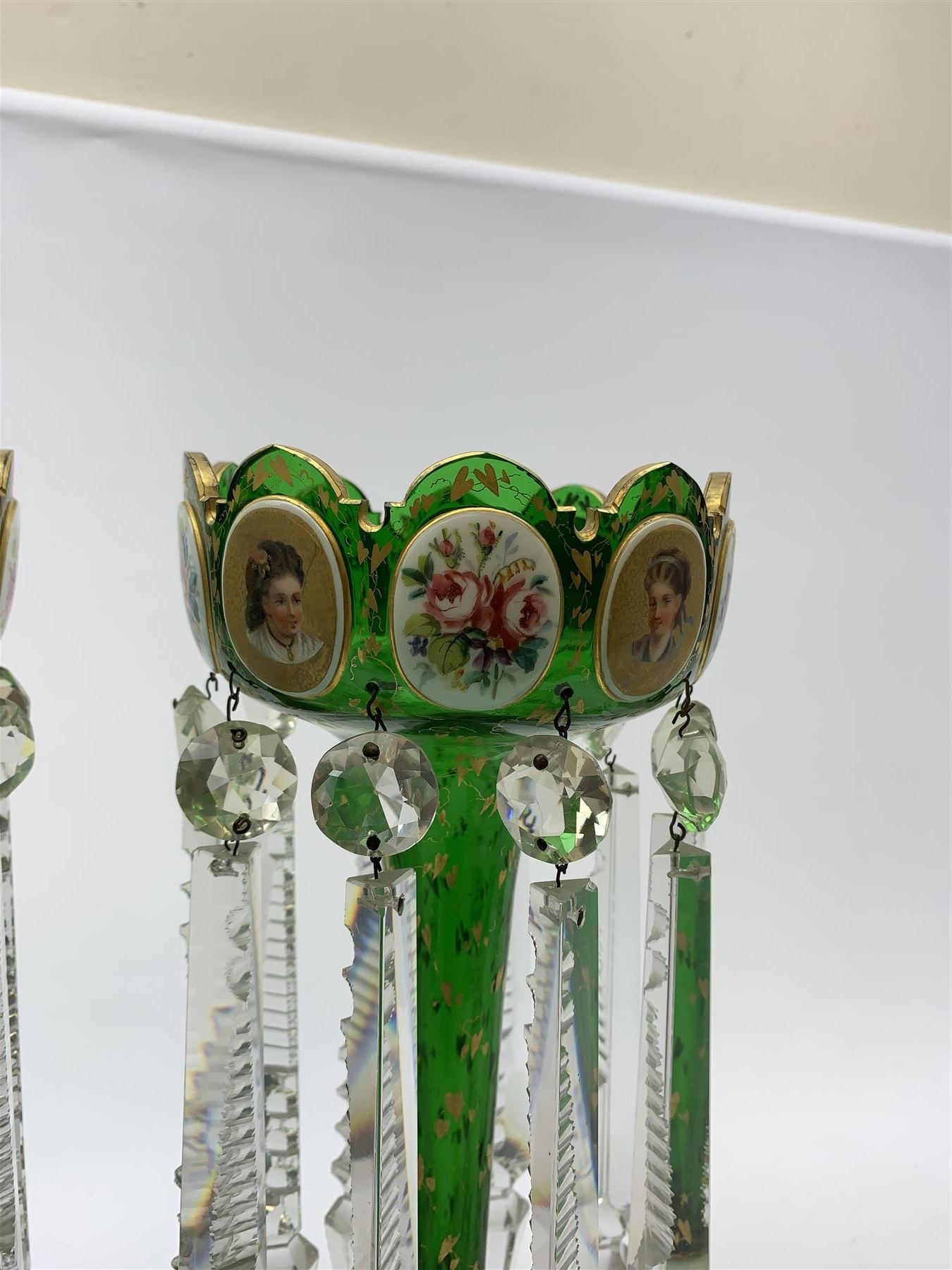 Pair of 19th century Bohemian green glass lustres, the castellated bowls decorated with overlaid panels of flowers and female portraits, upon tapering stems and overlaid spreading feet, heightened throughout with gilt, each supporting ten prismatic drops, H35cm