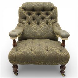 Late Victorian open armchair, in the manner of Howard & Sons, with deep buttoned seat and back upholstered in green damask fabric, with fringed detail to the lower arms, raised upon turned front legs with brass castors