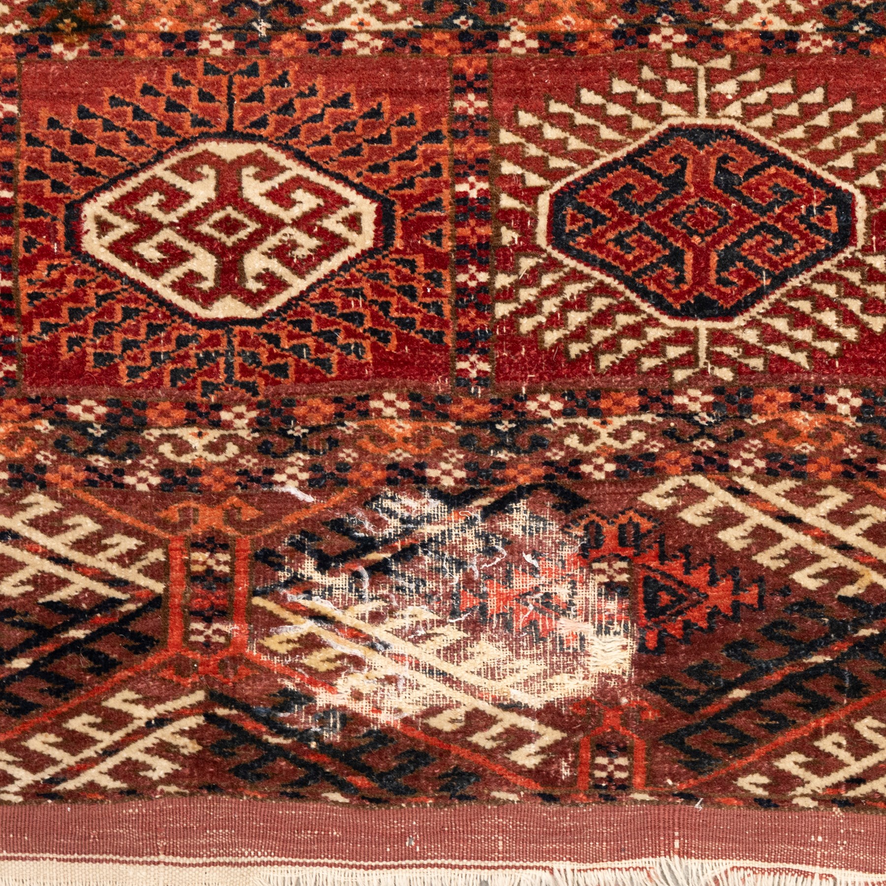 Persian Bokhara crimson ground rug, the field decorated with five rows of repeating Gul motifs with interspersed geometric design, enclosed by a guard band of further geometric-style Gul designs comprised of hook motifs