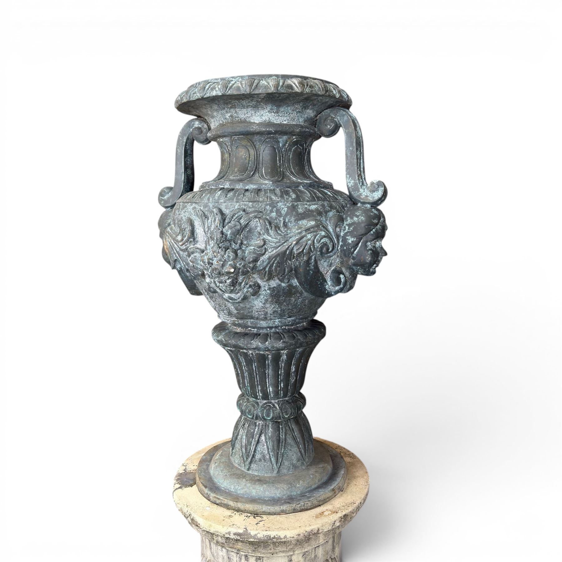 Large impressive Classical cast bronze center-piece urn, twin scroll handles with grape garlands, cherub masks and relief detail, raised on a circular cast stone pedestal with moulded detail